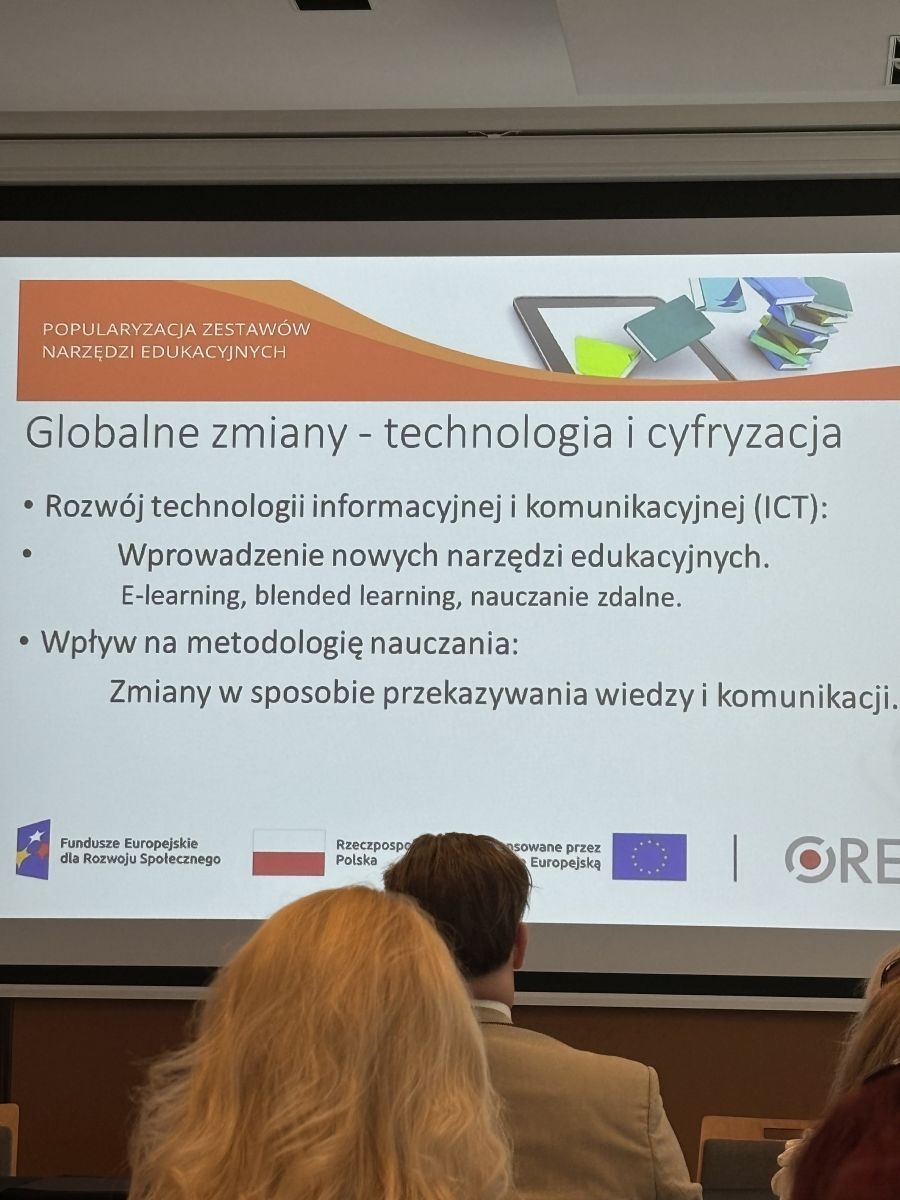 Na fotografii znajduje się powiększony slajd wyświetlany podczas konferencji dotyczący globalnych zmian  polagających na rozwoju technologii i cyfryzacji no wpływa na konieczność wprowadzenia nowych narzędzi edukacyjnych oraz mnetodologię nauczania. Zdjecie jest wykonane na Sali konferencyjnej, są widoczne dwie osoby siedzące przodem do wyświetlanego slajdu. 
